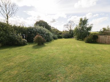 A large grassy garden with bushes trees and a wooden fence at Llain Haf in Llangefni