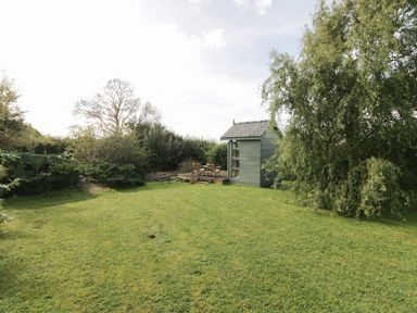 A small wooden shed with chairs on a deck surrounded by grass and trees at Llain Haf in Llangefni