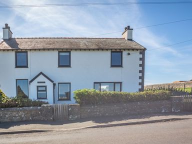 A two-story white house with dark window frames a hedge and a stone wall with a wooden gate at Tyn Y Berth in Benllech