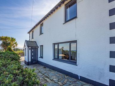 The exterior of a white house with multiple windows a dark door and a stone pathway with plants nearby at Tyn Y Berth in Benllech