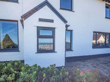 The exterior of a white building with multiple windows and plants in front at Tyn Y Berth in Benllech