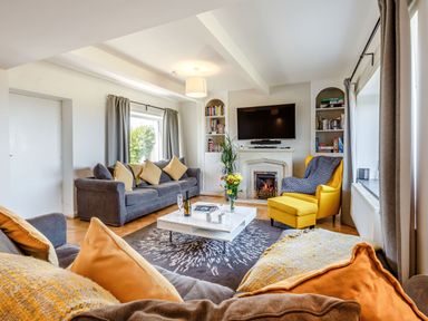 A living room with sofas, a yellow armchair, a white coffee table, and a fireplace with a TV above at Tyn Y Berth in Benllech