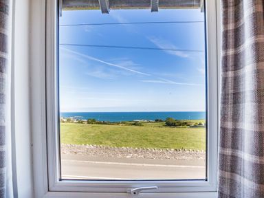 A window view showing a road stone fence grassy fields ocean and sky at Tyn Y Berth in Benllech