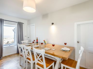 A dining room with a wooden table set with plates and glasses near a window with curtains at Tyn Y Berth in Benllech