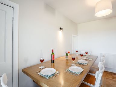 A dining room with a wooden table set with plates and glasses of wine at Tyn Y Berth in Benllech