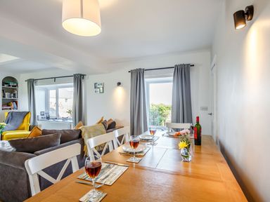 A dining table set with glasses of wine and plates next to a living area with a yellow armchair at Tyn Y Berth in Benllech