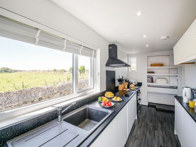 A kitchen with black countertops white cabinets a sink and various fruits on the counter at Tyn Y Berth in Benllech
