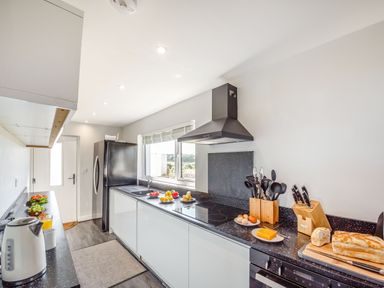 A kitchen with black refrigerator white cabinets black countertop utensils and food items at Tyn Y Berth in Benllech