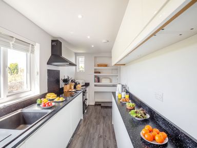 A kitchen with black countertops white cabinets and various fruits and food items on the counters at Tyn Y Berth in Benllech