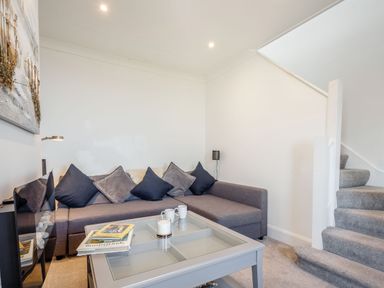 A living room with a gray corner sofa and cushions a glass coffee table with mugs and books a staircase with carpeted steps at Tyn Y Berth in Benllech