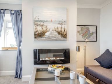 A living area with a glass coffee table books and candles by a wall-mounted fireplace and a sofa with a cushion at Tyn Y Berth in Benllech