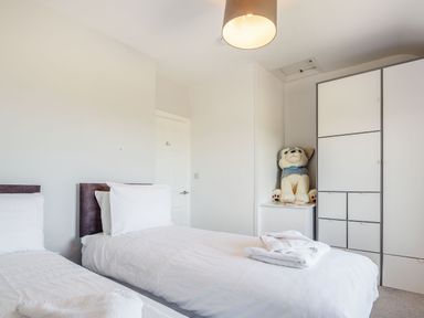 A bedroom with two single beds white bedding towels a stuffed animal on a cabinet and a white wardrobe at Tyn Y Berth in Benllech