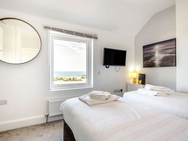 A bedroom with two beds stacked with towels a round mirror a window sea view a wall mounted tv a lamp and wall art at Tyn Y Berth in Benllech