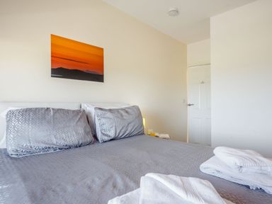 A bedroom with a bed covered in gray patterned bedding and pillows with white towels on it and a painting of an orange sunset on the wall at Tyn Y Berth in Benllech