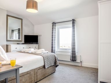 A bedroom with a double bed side table with glass of orange juice dresser with television window with plaid curtains at Tyn Y Berth in Benllech