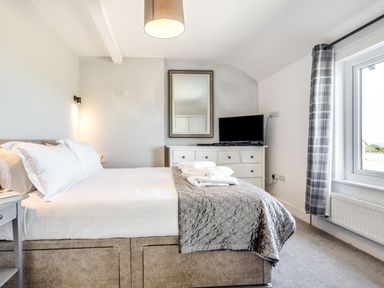 A bedroom with a bed white linens a dresser with a TV and a window with curtains at Tyn Y Berth in Benllech