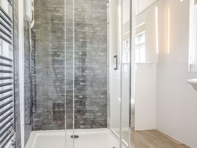 A shower with glass doors and gray tiled wall next to a heated towel rail at Tyn Y Berth in Benllech