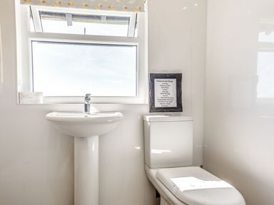 A bathroom with a pedestal sink, a toilet, and a window with a duck patterned blind at Tyn Y Berth in Benllech