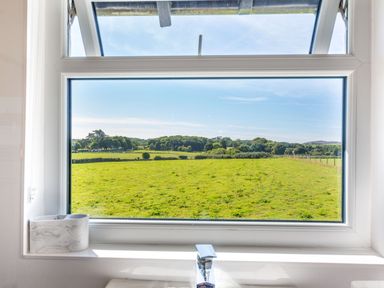 A window showing a green field and trees outside with a faucet and a container on the windowsill at Tyn Y Berth in Benllech