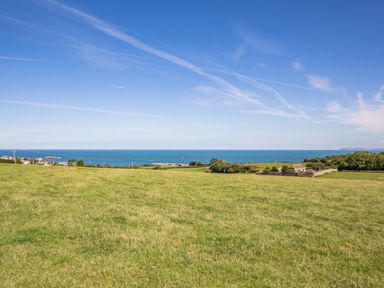 A grassy field with a stone building near the coast and blue ocean in the background at Tyn Y Berth in Benllech