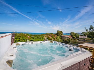 An outdoor hot tub with bubbling water near a garden with flowers and a sea view at Tyn Y Berth in Benllech