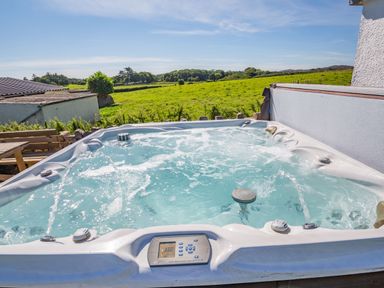 An outdoor hot tub with water jets and a digital control panel overlooking green fields and trees at Tyn Y Berth in Benllech