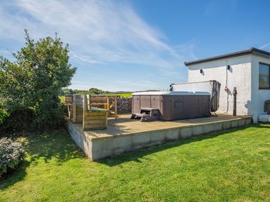 An outdoor patio with a hot tub and wooden benches next to a white building at Tyn Y Berth in Benllech