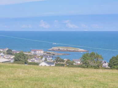 A coastal village with houses and trees near a body of water with an island and boats at Tyn Y Berth in Benllech