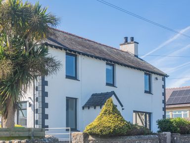 A white two-story house with black window frames a chimney and surrounding greenery at Tyn Y Berth in Benllech