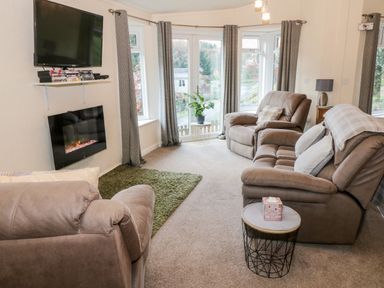 A living room with armchairs sofas a television and an electric fireplace at The Wee Lodge in Dollar