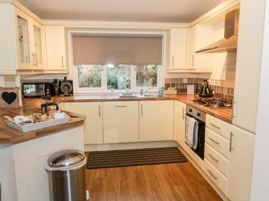 A kitchen with wooden countertops white cabinets a gas stove microwave coffee maker and window with a blind at The Wee Lodge in Dollar