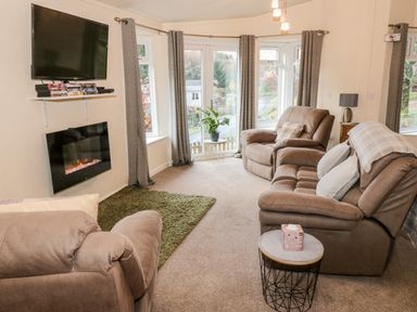 A living room with sofas a wall-mounted television and an electric fireplace at The Wee Lodge in Dollar