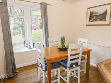 A dining area with a wooden table and four white chairs with cushions and a bowl of fruit on the table at The Wee Lodge in Dollar