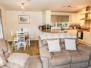 A living area with two beige sofas and a wooden dining table with white chairs near a kitchen at The Wee Lodge in Dollar