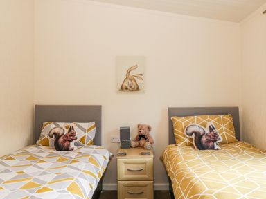 A bedroom with two single beds with geometric patterned bedding a nightstand with a teddy bear and a small painting on the wall at The Wee Lodge in Dollar