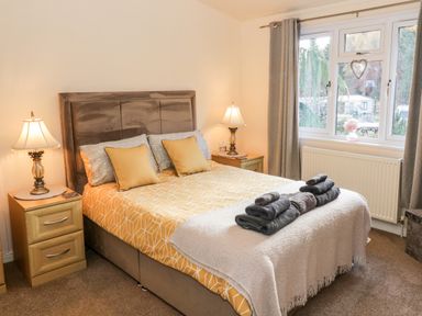 A bedroom with a bed with yellow bedding bedside tables and lamps in front of a window at The Wee Lodge in Dollar