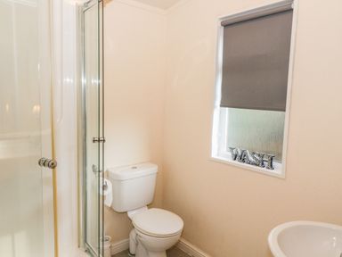 A bathroom with a toilet a shower with glass door a sink and a window with a grey blind and wash decoration at The Wee Lodge in Dollar