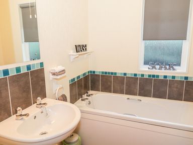 A bathroom with a white sink and bathtub with teal and brown tiles at The Wee Lodge in Dollar