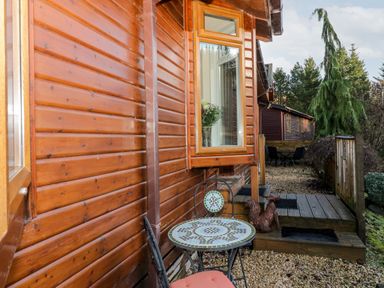 An outdoor seating area with a mosaic table and chairs next to a wooden cabin at The Wee Lodge in Dollar