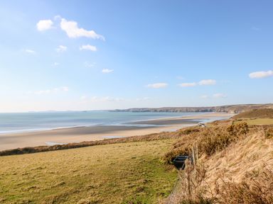 A coastal landscape with grassy fields and a sandy beach at Shepherds Hut - The Hurdle in Rosemarket
