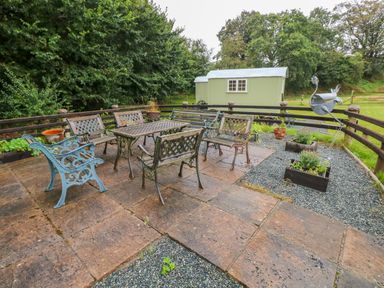 An outdoor patio area with metal chairs and tables surrounded by a wooden fence and greenery at Shepherds Hut - The Hurdle in Rosemarket