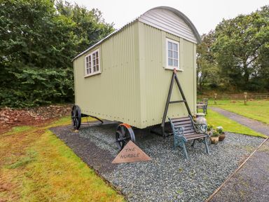 A green shepherds hut on wheels with benches and flower pots on gravel at Shepherds Hut - The Hurdle in Rosemarket
