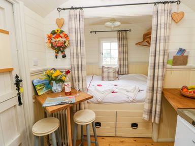 A compact room with a small table and stools a bed with folded towels and a window with curtains at Shepherds Hut - The Hurdle in Rosemarket