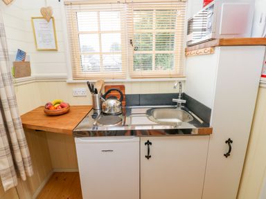 A small kitchen area with a sink stove microwave and fruit bowl at Shepherds Hut - The Hurdle in Rosemarket