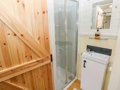 A bathroom with a wooden door a glass shower enclosure a white sink cabinet and a mirror at Shepherds Hut - The Hurdle in Rosemarket