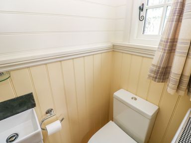 A corner of a bathroom with a toilet sink window and plaid curtains at Shepherds Hut - The Hurdle Rosemarket