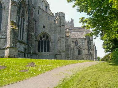An old stone church with arched windows next to a pathway and green grassy area with trees at 32 Cranleigh Close in Tuckton