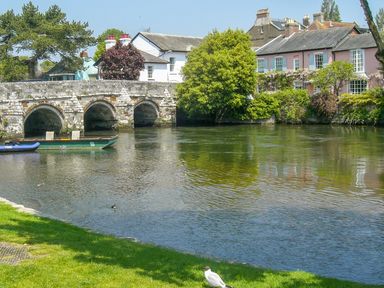 A river with boats and a stone bridge near houses and trees at 32 Cranleigh Close in Tuckton