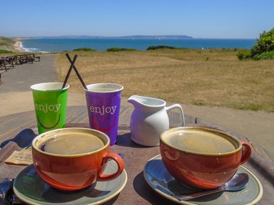 Two cups of coffee on a table with two paper cups and a milk jug with a view of the sea at 32 Cranleigh Close in Tuckton
