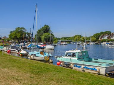 Boats moored along a river with houses and trees in the background at 32 Cranleigh Close in Tuckton